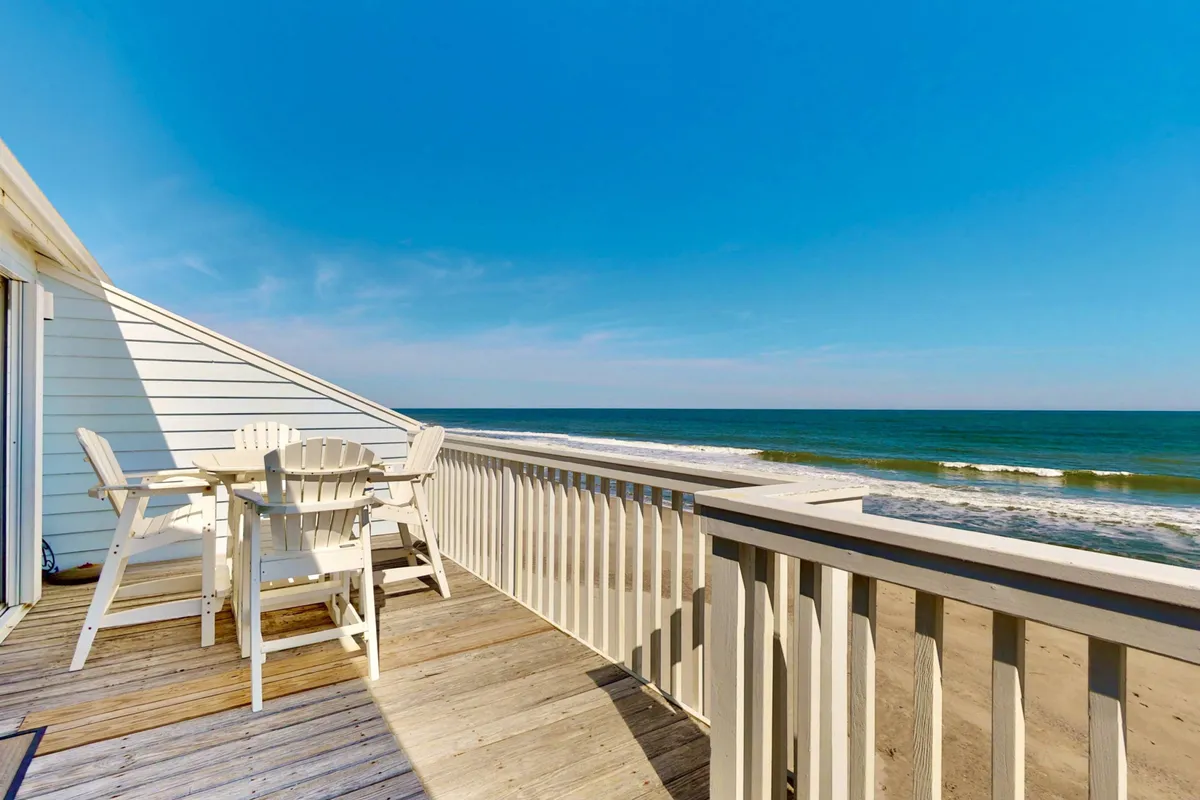 A private, top-floor deck with a table and chairs overlooking the endless blue ocean. The deck features a sturdy railing and is an inviting space for al fresco dining, morning coffee, or evening relaxation while soaking up the sounds of the surf.