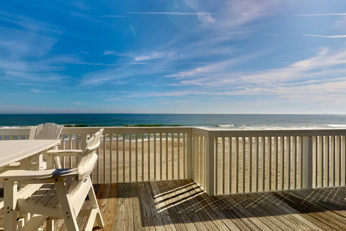A relaxing beachfront deck furnished with comfortable seating and dining furniture overlooks the shimmering ocean and sandy beach. The inviting space is ideal for group gatherings or family breakfasts, with the expansive view setting the stage for memorable mornings or sunset dinners together.
