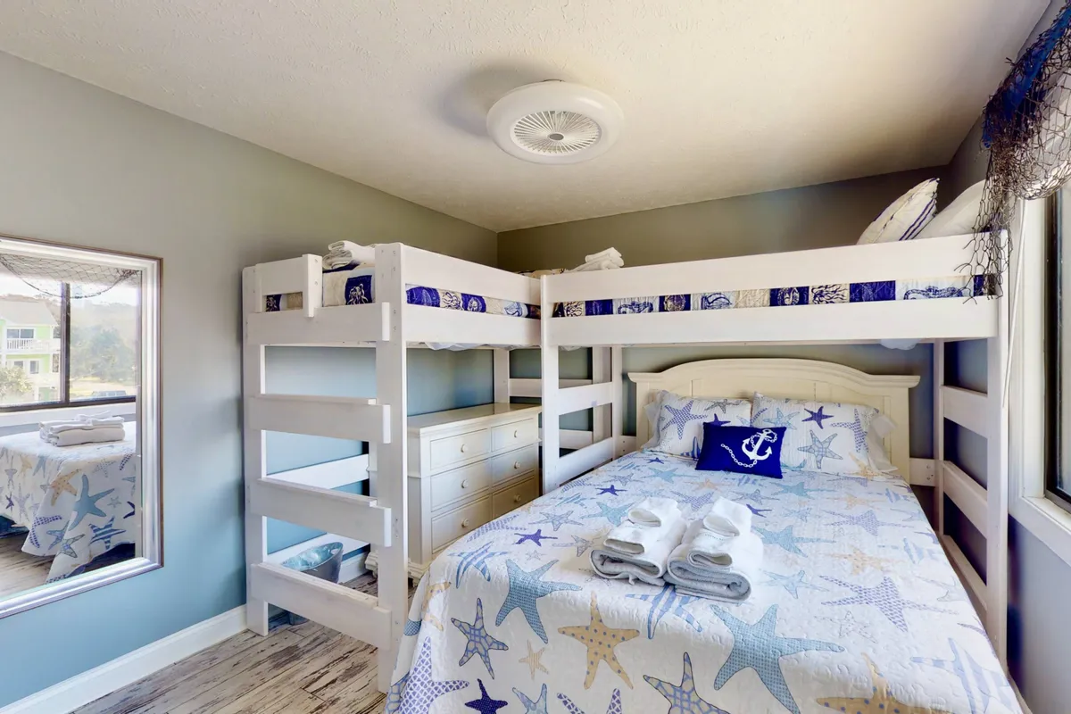 A playful and cozy second bedroom setup featuring a bunk bed and a double bed adorned with decorative pillows. A mirror reflects the room, enhancing the sense of space, and the décor suggests a family-friendly environment ideal for children and adults alike.