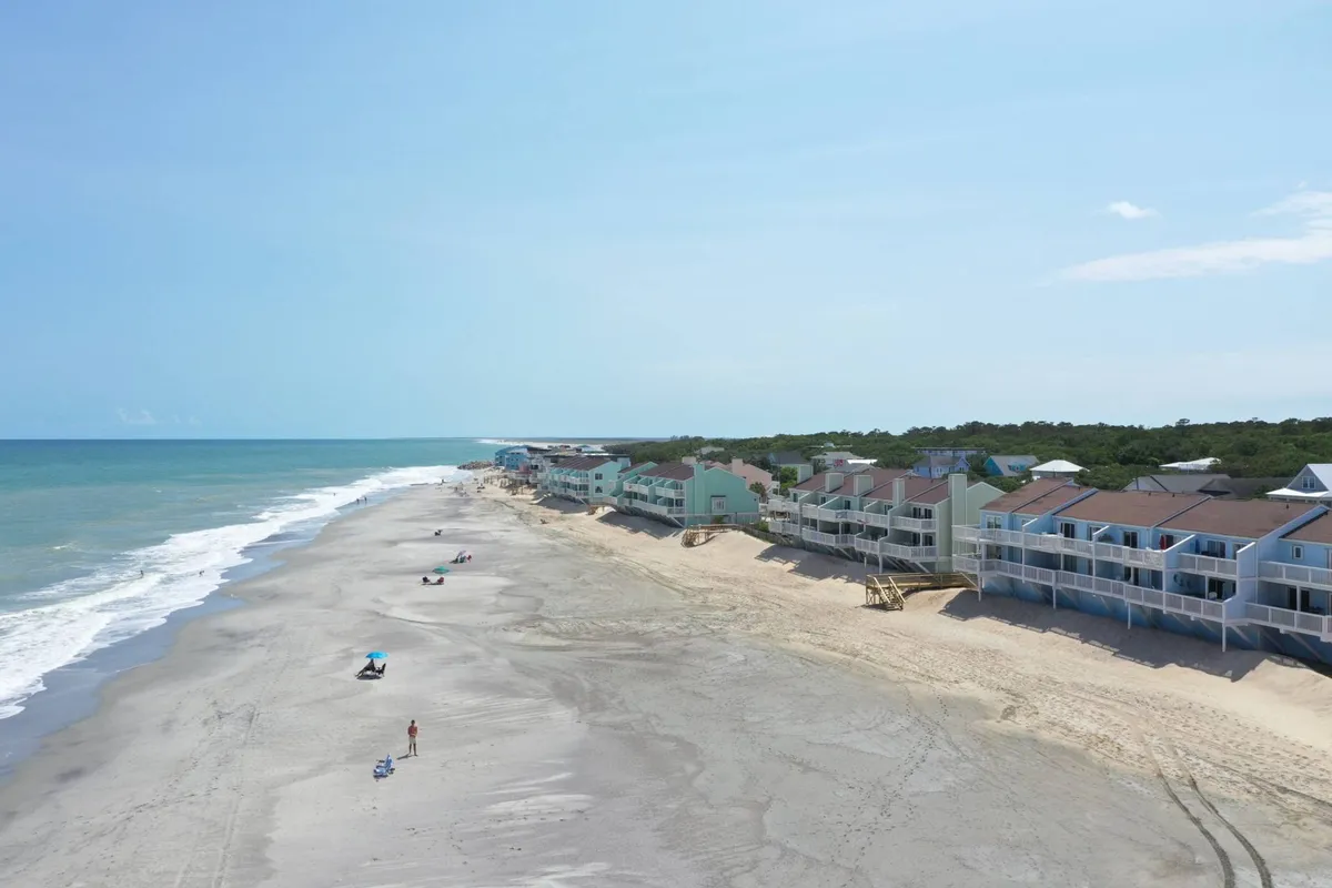 A lively stretch of beachfront with people enjoying the sand and surf, bordered by beachfront properties. The scene includes waves rolling onto the shore and the inviting expanse of sand, suggesting opportunities for sunbathing, swimming, and community fun steps from the condo.