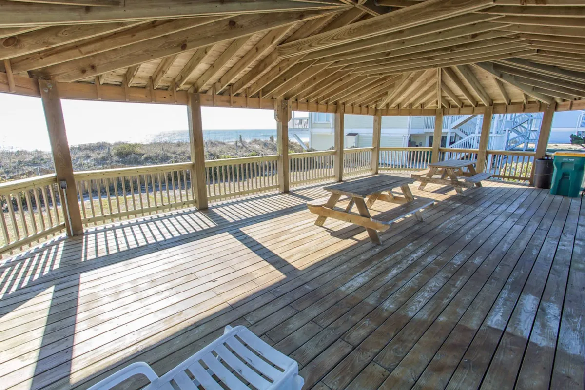 A spacious outdoor area featuring several wooden picnic tables and open space that encourages group activities and socializing. The scenic view in the background, combined with the ample seating, makes it an inviting spot for family picnics, games, or simply relaxing after a day of adventure.