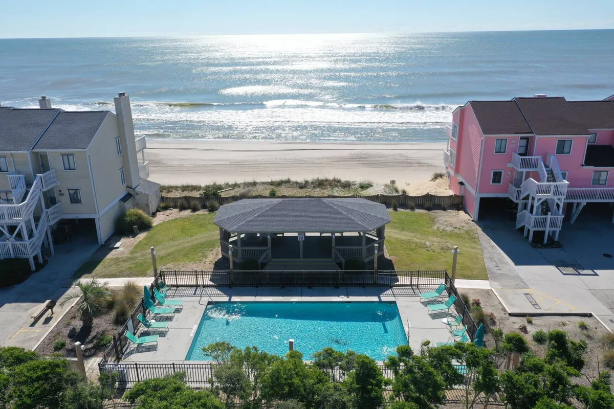 A tranquil outdoor swimming pool sits at the center, framed by a charming gazebo, with glimpses of the ocean and the resort's surrounding buildings in the background. The inviting pool area is set up for both relaxation and recreation, offering lounge spots for sunbathers and shaded seating under the gazebo.
