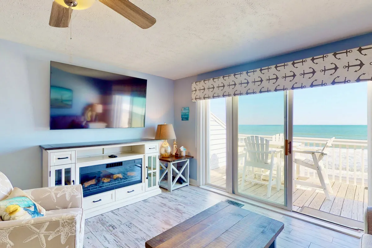 A cozy living room featuring a plush couch set in front of a large TV and fireplace, with glass doors opening to reveal breathtaking ocean views. The setup is perfect for relaxing, watching movies, or enjoying the scenery.