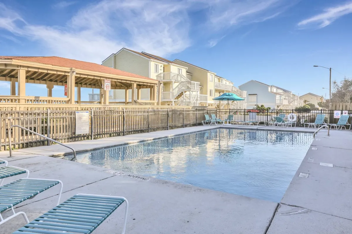 This image captures a vibrant outdoor pool scene within the resort community, featuring a sparkling swimming pool surrounded by lounge chairs, a cabana, and adjacent buildings. The area is bathed in sunlight, inviting families to swim, relax, and enjoy social gatherings.